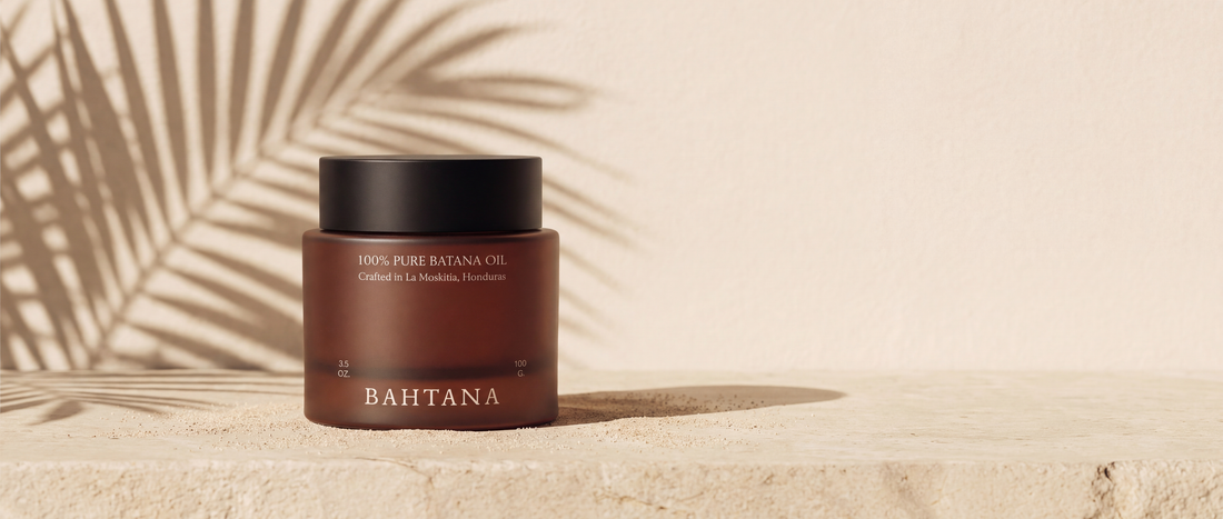 A jar of BAHTANA raw batana paste on warm sand under palm shadow