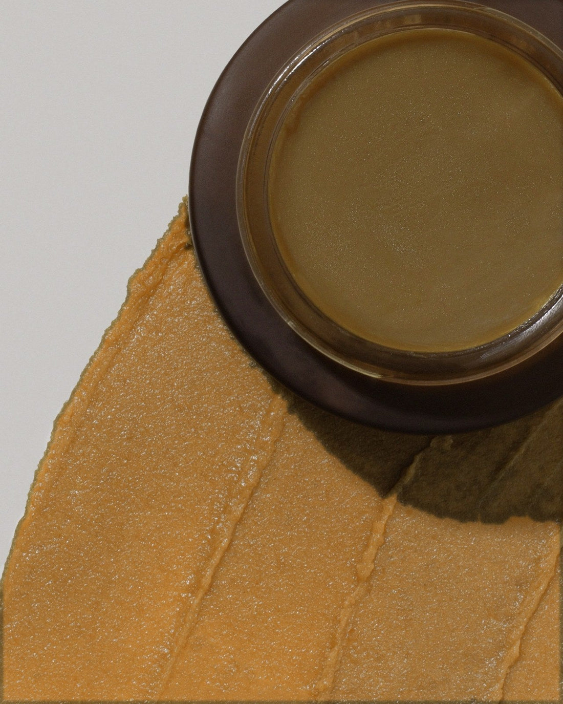 A jar of BAHTANA raw batana beside a swatch of the caramel-colored paste